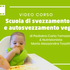 Bambino in seggiolone, con bavaglino verde, che mangia con le mani. Titolo: "Scuola di svezzamento e autosvezzamento veg".