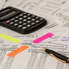 Kalkulator i dokumenty finansowe. Na jednym z nich zaznaczono "DON'T FORGET THE TAX IMPLICATION", co może dotyczyć np. podatek od gruntów rolnych poniżej 1 ha.