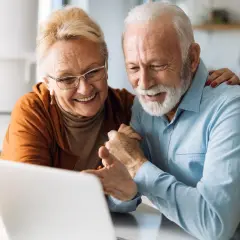 Uśmiechnięta para seniorów korzystająca z laptopa.