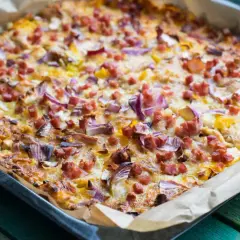Herzhafte pizza ohne kohlenhydrate mit Speck und roten Zwiebeln, frisch aus dem Ofen auf Backpapier.