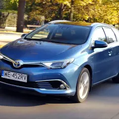 Niebieski Toyota Auris 1.8 VVT-i Hybrid w wersji kombi jedzie po drodze w otoczeniu jesiennych drzew.