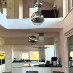Nowoczesne lampy loftowe w kształcie kul wiszą nad białą kuchnią z wyspą.