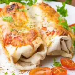 Dwa zapieczone burrito z kurczakiem, polane ciągnącym się serem, podane z pomidorkami koktajlowymi i natką pietruszki.
