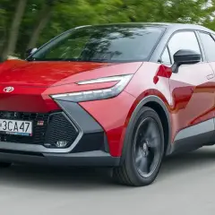 Czerwona Toyota C-HR 2020 z czarnym dachem pędzi po drodze, otoczona zielenią drzew.