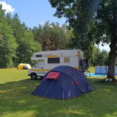 Namiot i kamper na trawie, w tle las i basen. Idealne miejsce na **camping Świętokrzyskie**.