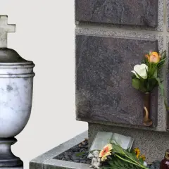 Kamienna urna z krzyżem i kwiaty przy ścianie kolumbarium.