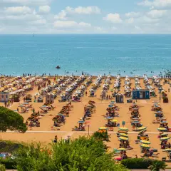 Una spiaggia affollata vicino a Venezia, con file ordinate di ombrelloni gialli e bianchi e persone che si godono il sole e il mare azzurro.