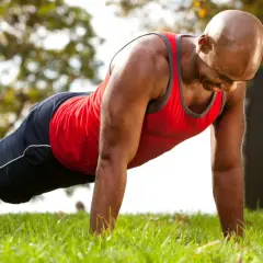 Homme chauve en tenue de sport faisant un exercice bras sur l'herbe.