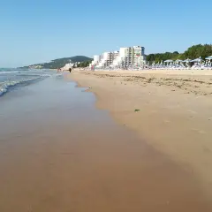 Piękna plaża w Albena Bułgaria. Fale obmywają piaszczysty brzeg, a w oddali widać hotele i rzędy parasoli.