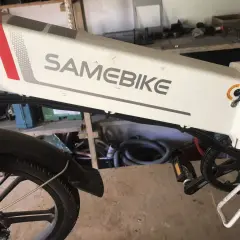 Biały rower elektryczny SAMEBIKE, z czerwonym i szarym paskiem, stoi w warsztacie. Wspomaganie nie działa, co jest frustrujące.