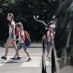 Dwoje dzieci, pieszy na pasach, z plecakami przechodzi przez ulicę.