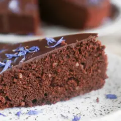 Ein Stück saftiger schokokuchen ohne zucker, garniert mit blauen Kornblumenblättern auf einem Teller.