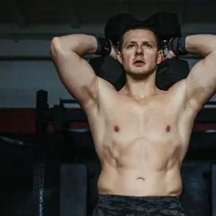 Mężczyzna ćwiczy z hantlami nad głową w siłowni.