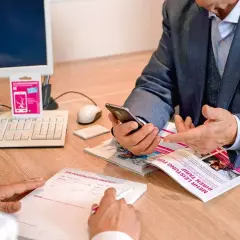 Mężczyzna w garniturze sprawdza telefon, być może szukając informacji, jak sprawdzić kod PIN w telefonie, podczas rozmowy z doradcą.