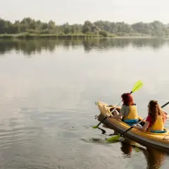 Dwie dziewczyny na kajaku, odkrywają roztocze atrakcje dla dzieci. Spokojna tafla wody i zielone brzegi tworzą idealne tło do wodnych przygód.