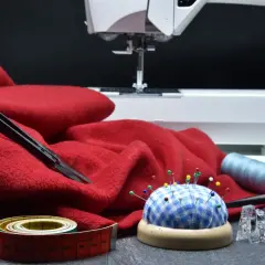 Czerwony materiał, maszyna do szycia, szpilki, miarka i nożyczki – wszystko gotowe do tworzenia patchwork projektów.