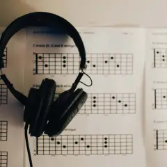 Słuchawki wiszą na arkuszach z diagramami akordów gitarowych, idealne do kształcenia słuchu i nauki gry.