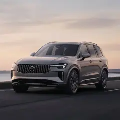 Elegancki Volvo XC90 T8 w kolorze szarym jedzie wzdłuż malowniczego wybrzeża o zachodzie słońca.