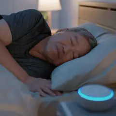 Ein Mann schläft tief und fest im Bett. Neben ihm leuchtet ein Smart Speaker, der ihm hilft, lange schlafen zu können.