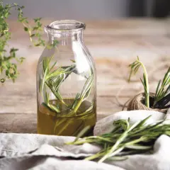 Aceite de romero infusionado en botella, ideal para el alopecia femenina tratamiento natural. Hierbas frescas y tijeras a un lado.