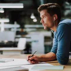 Junger Mann mit Kopfhörern, der konzentriert an einem Entwurf für sein Grafik Design Studium arbeitet.
