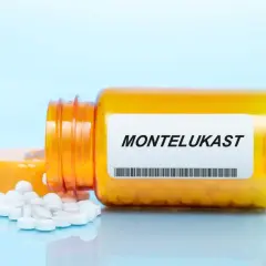Pomarańczowa butelka z tabletkami montelukast, kilka białych tabletek rozsypanych obok.