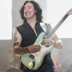 Jan Borysewicz z Lady Pank gra na gitarze, uśmiechając się do publiczności.