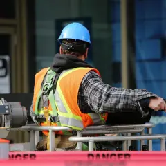 Operaio con giubbotto ad alta visibilità e il suo blu, il colore del casco cantiere, spicca tra le attrezzature.