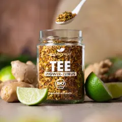 Glas mit Ingwer-Zitrus-Tee, frischem Ingwer und Limetten. Perfekt für einen wärmenden Tee, der lange ziehen kann.