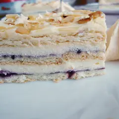Pyszna Pani Walewska bez pieczenia, z kremem i jagodami, posypana płatkami migdałów. Obok beza.