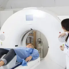 Pacjentka leży na stole aparatu do badań obrazowych, gdzie lekarz przygotowuje się do wykonania koronarografii.