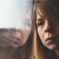 Portret kobiety z widocznym odbiciem w szybie, sugerującym refleksję lub rozdwojenie.