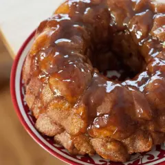 Delizioso monkey bread dorato, ricoperto di glassa lucida, servito su un piatto con bordo rosso.