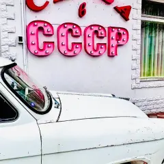 Biały, stary samochód przed budynkiem z neonem CCCP. Czy to podróż w czasie do tamtych lat?