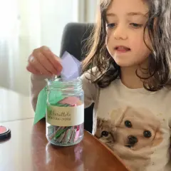 Bambina inserisce un bigliettino nel barattolo "Scaccia-Noia", pieno di idee per giochi da fare quando ci si annoia.