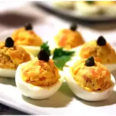 Six oeufs mimosa saumon garnis d'une olive noire sur une assiette blanche.