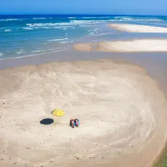 Dos personas descansan bajo una sombrilla a rayas en una playa de arena en Ria Formosa. El mar azul y las aguas cristalinas rodean la isla.