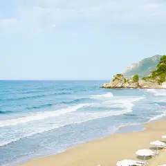 Piękna, piaszczysta plaża na Korfu z rzędami białych parasoli i turkusowym morzem.