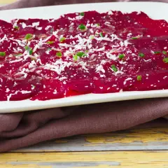 Rote Bete Carpaccio, hauchdünn geschnitten und mit Parmesan und Schnittlauch bestreut, auf einem weißen Teller.