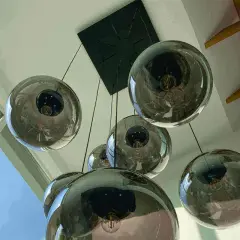 Un grupo de lámparas bola colgante de cristal ahumado cuelgan de un techo blanco, reflejando la luz y el entorno.