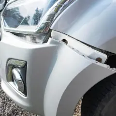 Le bouclier avant de la voiture est détaché, révélant des fixations et le pneu.