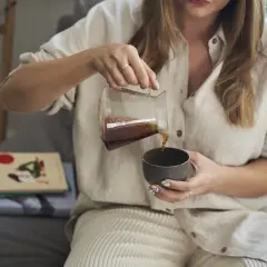 Kobieta nalewa kawę z drippera do filiżanki, ciesząc się chwilą relaksu.
