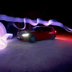 Czerwony samochód w nocnej scenerii, otoczony fioletowymi i różowymi smugami światła, efekt **panning**.