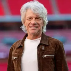 Jon Bon Jovi w brązowej kurtce, uśmiechnięty. Fani marzą o jego **bon jovi koncerty 2026**.