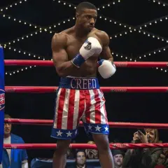 Michael B. Jordan jako Adonis Creed w szortach w barwach USA, gotowy do walki. W tle widać Sylvestra Stallone. Creed II obsada w akcji.