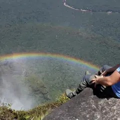 Mężczyzna siedzi na skale przy wodospadzie Salto Ángel, podziwiając tęczę.