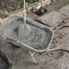 Taczka z betonem i łopatą, gotowa do wylania ławy fundamentowej. Wymiary ławy fundamentowej są kluczowe dla stabilności konstrukcji.