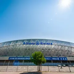 Nowoczesny stadion Allianz Riviera w Nicei, z charakterystycznym, przeszklonym dachem i niebieskim napisem.