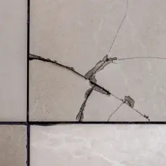 Gros plan sur un carrelage de sol beige avec une fissure importante. Il faut réparer cette fissure pour éviter qu'elle ne s'aggrave.