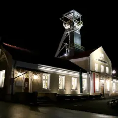 Wieczorem przy szybie kopalni Wieliczka, gdzie można kupić bilety, widać oświetlone budynki i wieżę wyciągową.